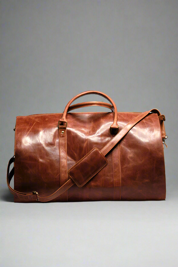 A brown premium top-grain leather duffle bag with dedicated compartments for suits, shoes, ties, and essentials, displayed in a flat position with the capacity to stand upright.