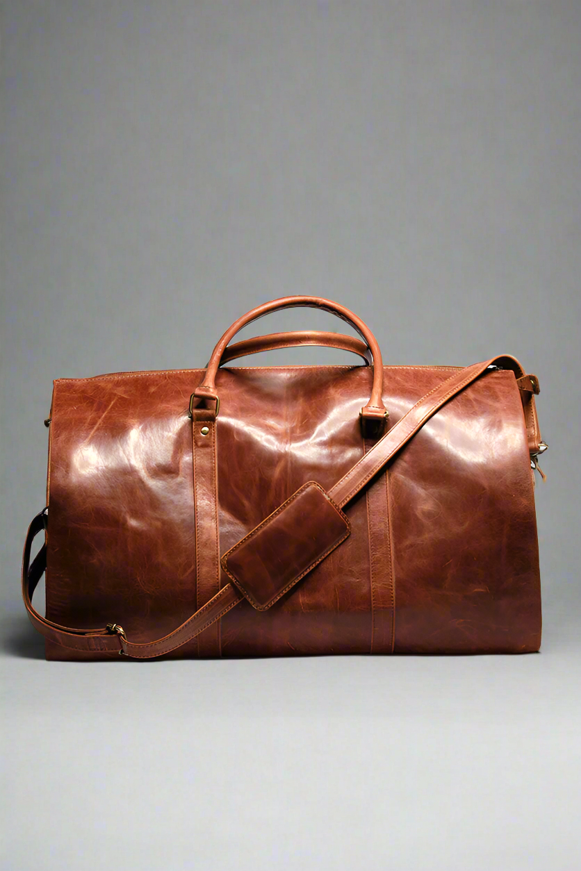 A brown premium top-grain leather duffle bag with dedicated compartments for suits, shoes, ties, and essentials, displayed in a flat position with the capacity to stand upright.