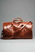 A brown premium top-grain leather duffle bag with dedicated compartments for suits, shoes, ties, and essentials, displayed in a flat position with the capacity to stand upright.
