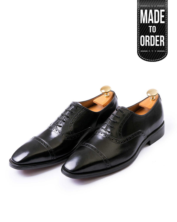 A pair of black leather brogues with lace-up closure and a gold-tone buckle, displayed against a white background with a 'Made to Order' label.