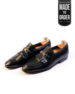A pair of black leather moccasin shoes with a metal buckle on the top, displayed against a white background with a 'Made to Order' label on the top right.