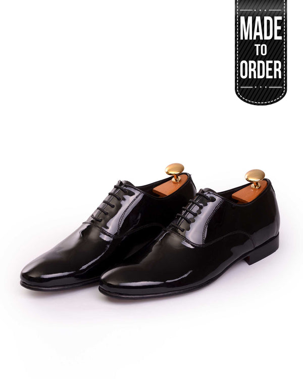 A pair of black patent leather lace-up shoes with a glossy finish and metal pins on the heel.