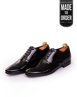 A pair of black patent leather lace-up shoes with a glossy finish and metal pins on the heel.