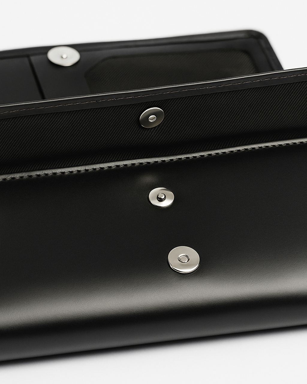 Close-up of a black clutch bag with silver buttons on a white background