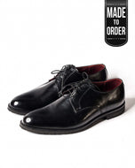 A pair of black leather oxford shoes with a lace-up closure and a V-shaped toe.