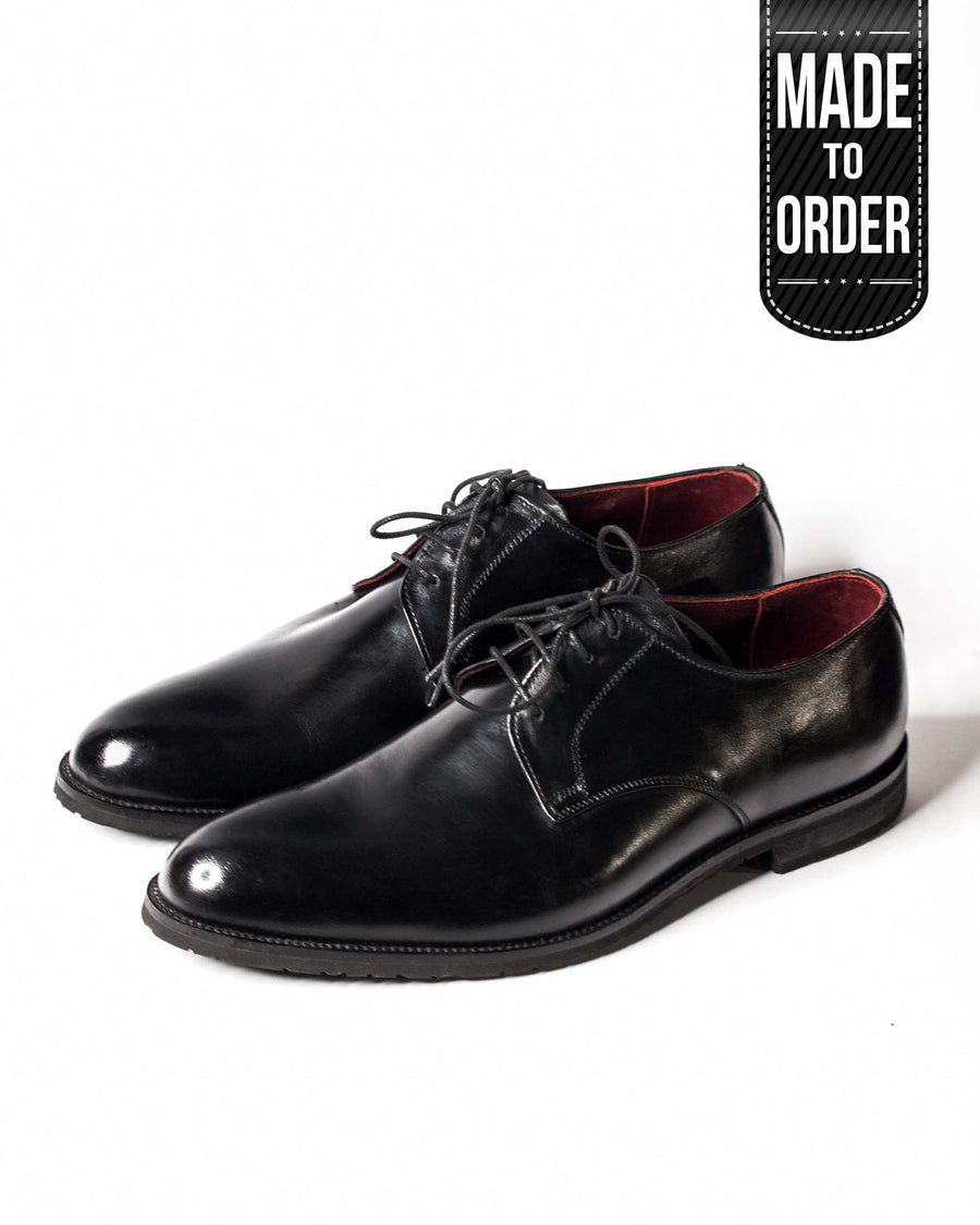 A pair of black leather oxford shoes with a lace-up closure and a V-shaped toe.