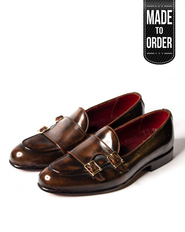 A pair of brown double strap monk style burnished loafers with a high gloss finish.