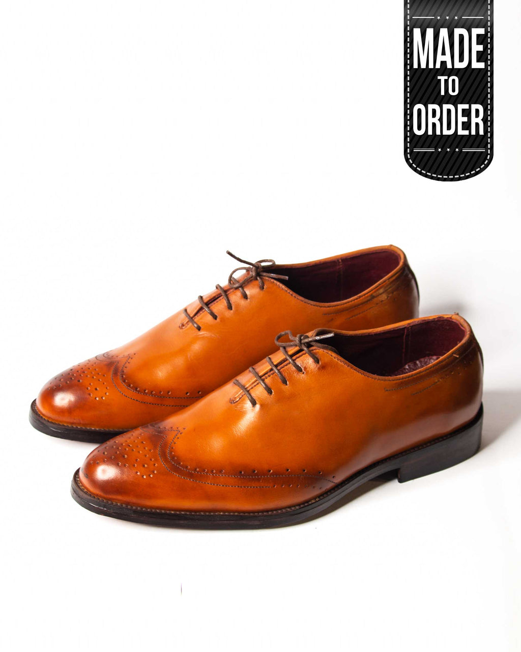 A pair of brown Wholecut Wingtip dress shoes with a lace-up closure, displayed against a white background with a 'made to order' label.